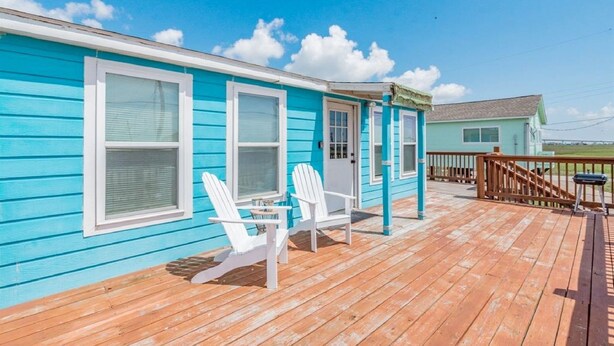 A turquoise house with a wooden deck, two white Adirondack chairs, and a small table.