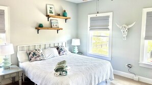 Ein Schlafzimmer mit einem Bett, Nachttischen, einer Lampe, einem Fenster mit Jalousien und Wanddekorationen, darunter ein Schädel und gerahmte Bilder.