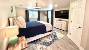 Une chambre à coucher avec un lit, une commode, un téléviseur et une porte.