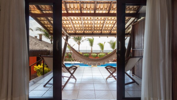 A view of a pool area with a hammock, two lounge chairs, and a thatched roof structure. - Casa do Mar praia de Cotovelo Carpediem (Parnamirim)