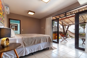 A bedroom with a bed, a small table, and a view of a balcony with outdoor furniture. - Casa do Mar praia de Cotovelo Carpediem (Parnamirim)