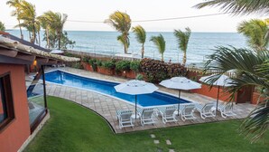 A swimming pool with lounge chairs and umbrellas, surrounded by palm trees and a view of the ocean. - Casa do Mar praia de Cotovelo Carpediem (Parnamirim)