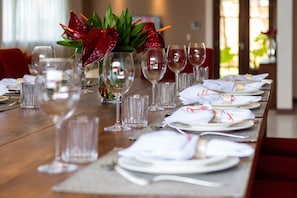 A dining table set with white plates, glasses, and a centerpiece of red flowers. - Casa do Mar praia de Cotovelo Carpediem (Parnamirim)