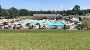 A large outdoor swimming pool surrounded by lounge chairs and umbrellas, with a building in the background. - Lake view retreat steps to Badin Lake! Pool, Beach, Restaurant/Bar & Boat Launch (New London)