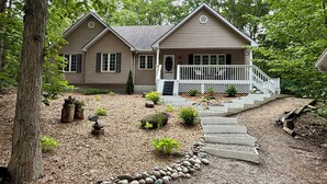 A two-story house with a front porch, a stone pathway leading to the entrance, and a small garden with various plants and rocks. - Former Lottery Home Near Private Beach & River (Grand Bend)