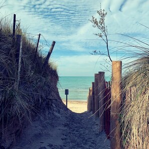 A beach path leading to the sea with a wooden fence and a signpost.