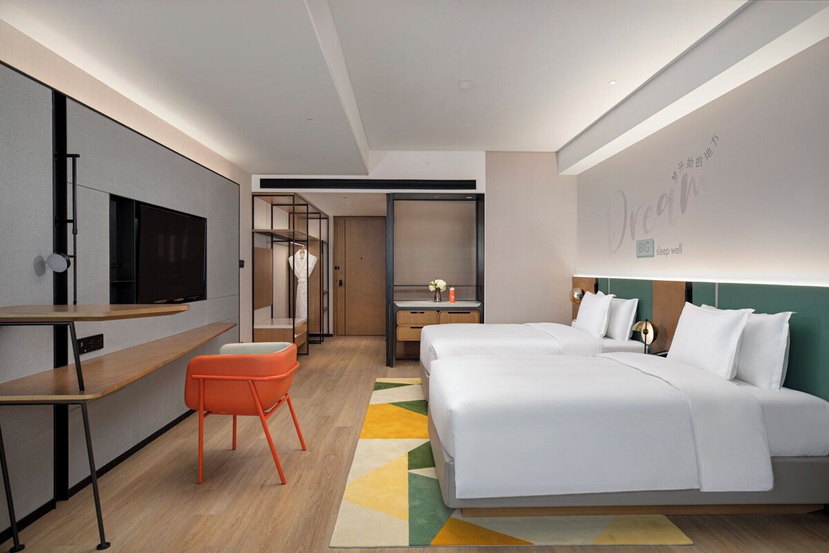 A modern hotel room with a large bed, a desk with a flat-screen TV, a seating area, and a walk-in closet.