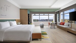 A modern hotel room with a large bed, a sofa, a small table, and a city view. - EVEN Chengdu Jinniu by IHG (Chengdu)