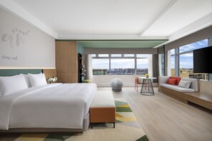A modern hotel room with a large bed, a sofa, a small table, and a city view. - EVEN Chengdu Jinniu by IHG (Chengdu)