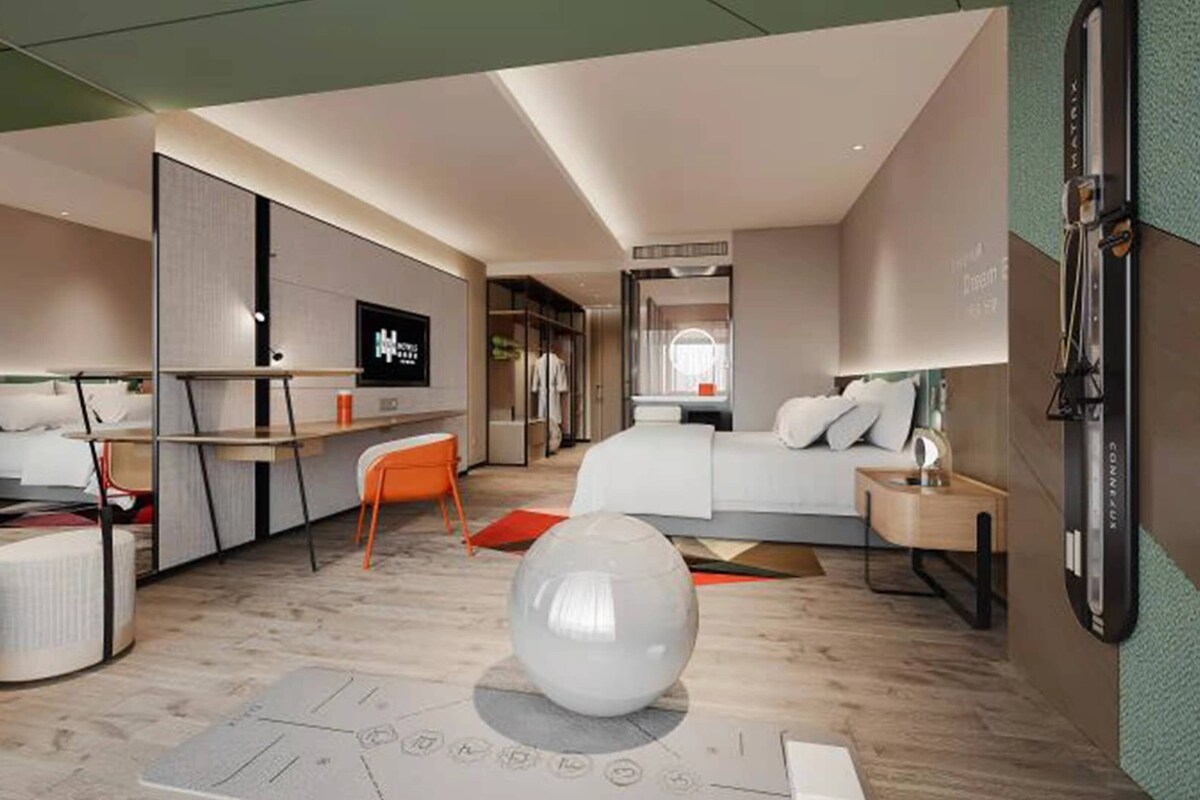 A modern hotel room with a bed, a desk, a chair, and a television.