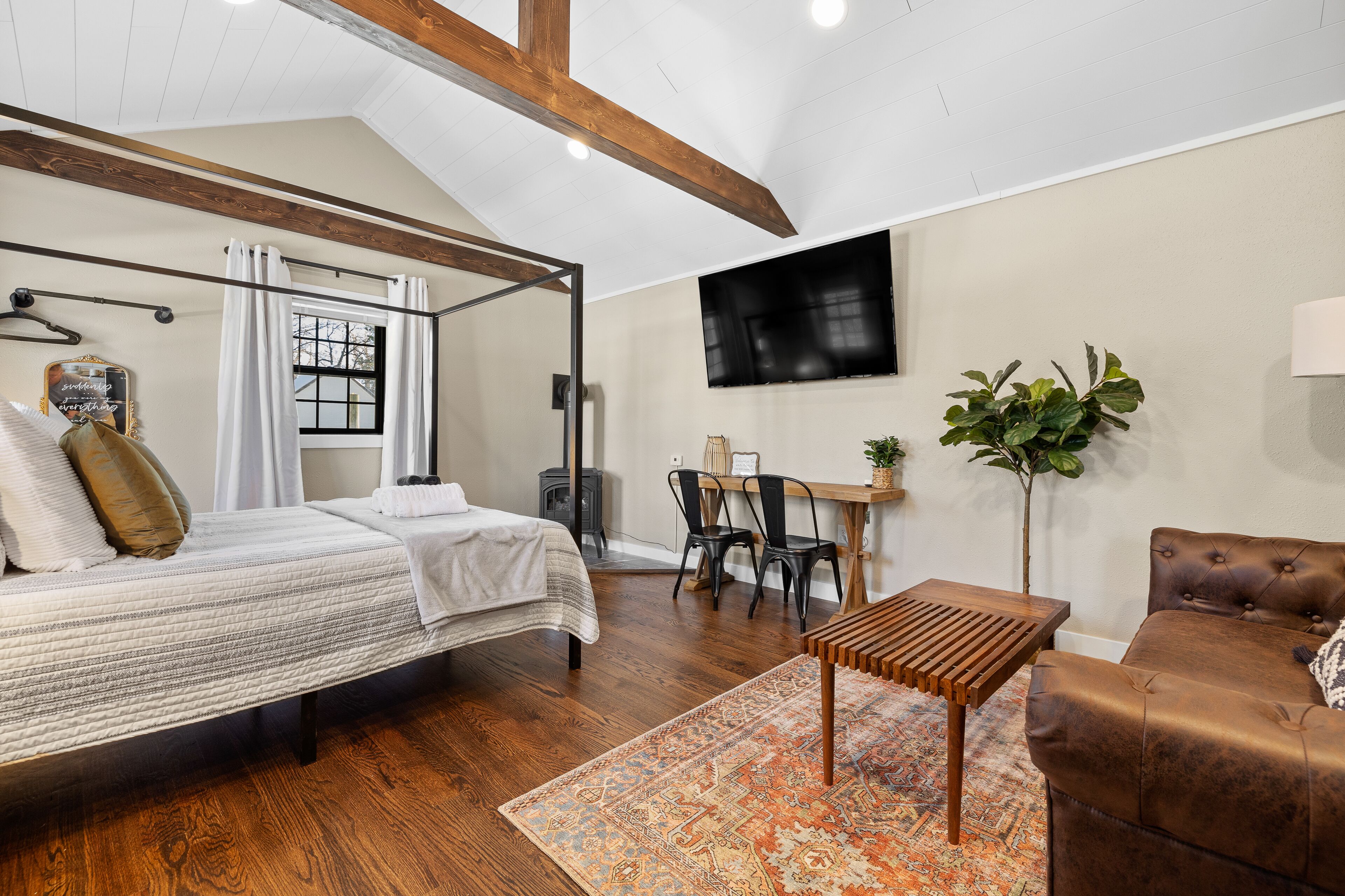 Ein Schlafzimmer mit Himmelbett, Schreibtisch, Stuhl, Sofa und einem Fernseher an der Wand.
