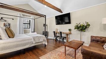 Ein Schlafzimmer mit Himmelbett, Schreibtisch, Stuhl, Sofa und einem Fernseher an der Wand.