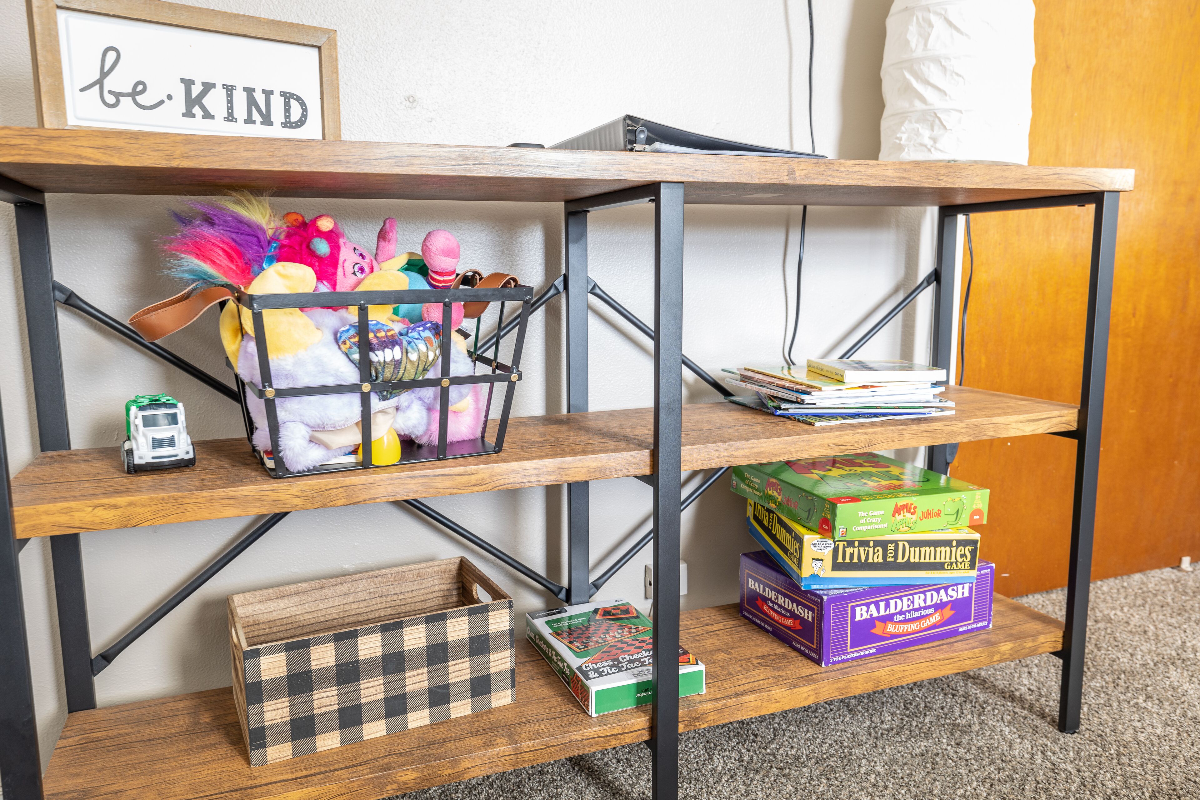 A wooden shelf unit with a 'be KIND' sign, holding various board games and a toy car.