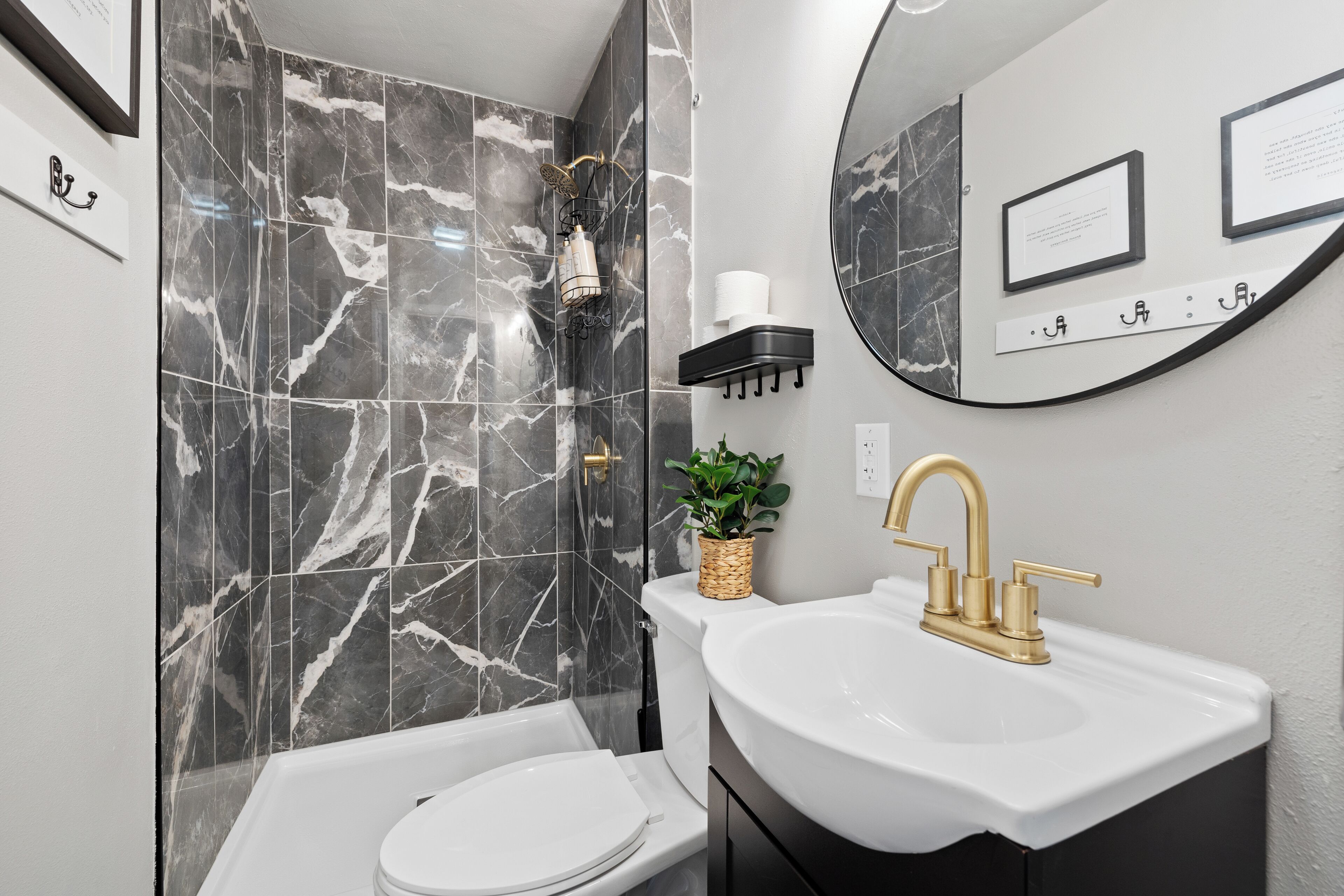 A modern bathroom with a white toilet, a gold faucet sink, and a shower with a marble wall.