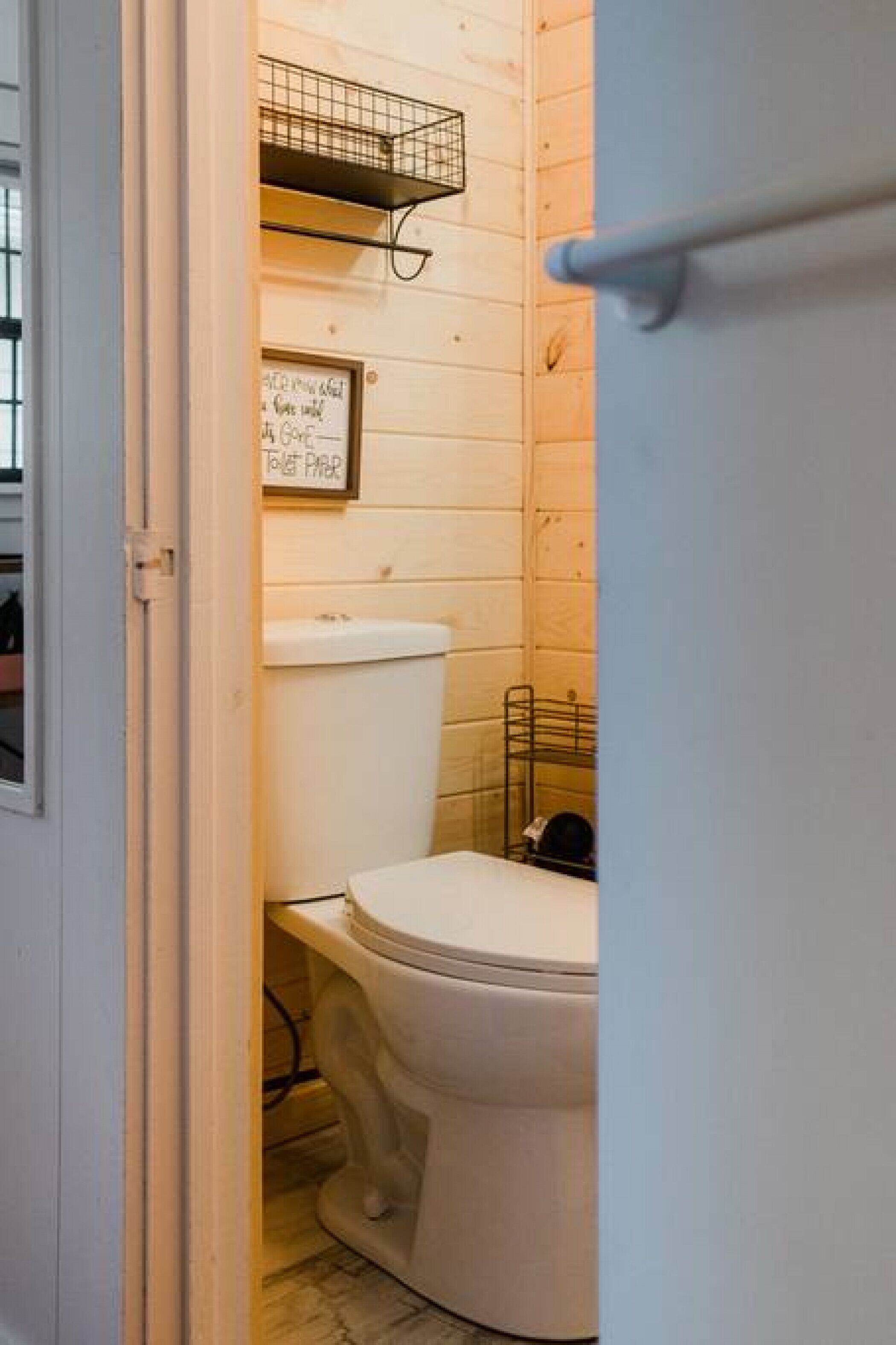A small, compact bathroom with a toilet, a shelf above the toilet, and a sign on the wall.