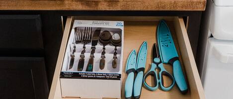 Een keukenblad met een waterfles in teal, een gasfornuis en een lade met bestek en scharen.
