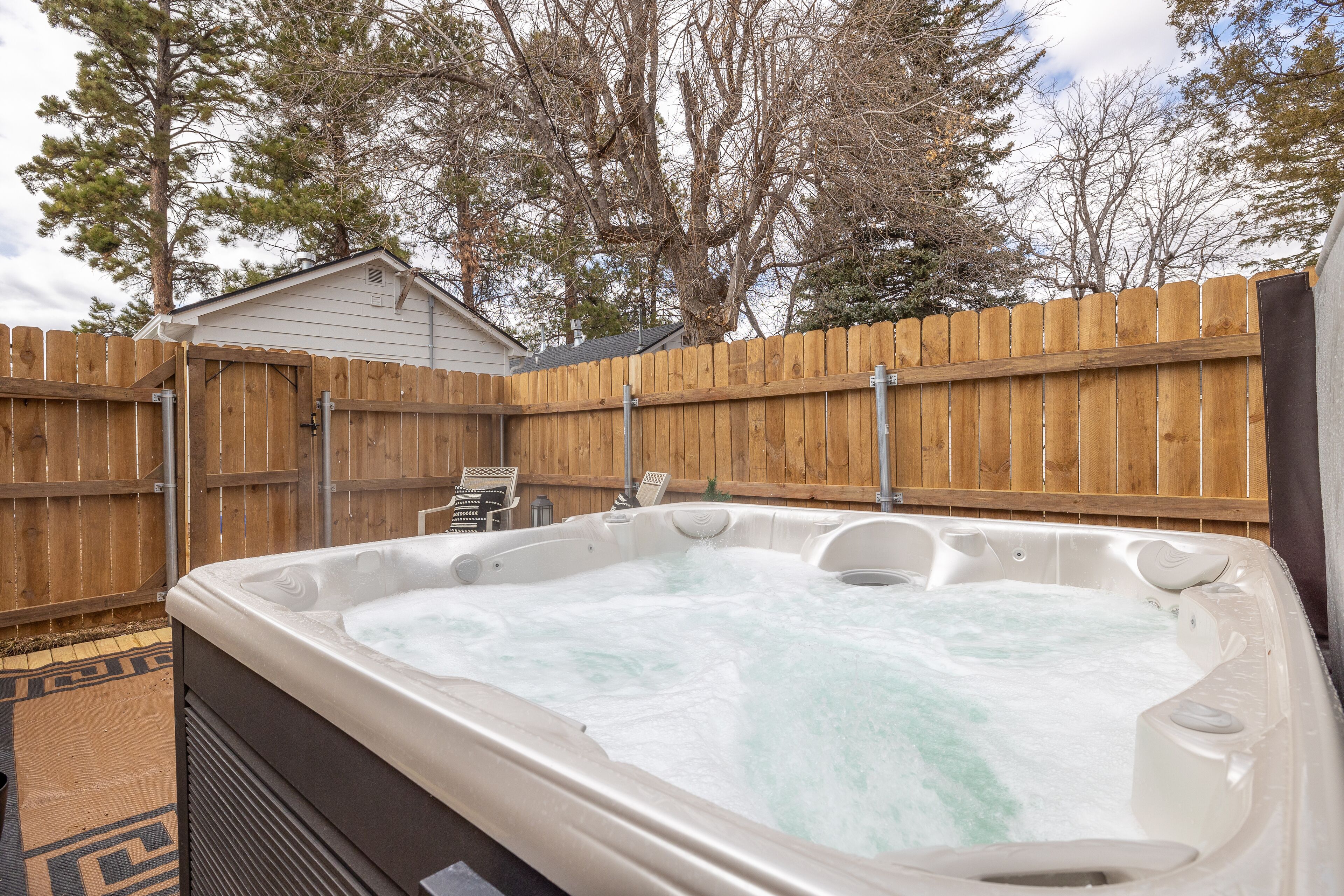 Un jacuzzi en un patio trasero con cerca de madera, una silla y un cobertizo pequeño.