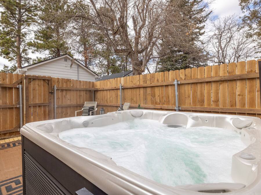 Un jacuzzi en un patio trasero con cerca de madera, una silla y un cobertizo pequeño.