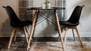 A small dining area with a table and two chairs, a potted plant, and a window with curtains. - Spearfish Cottages (Spearfish)
