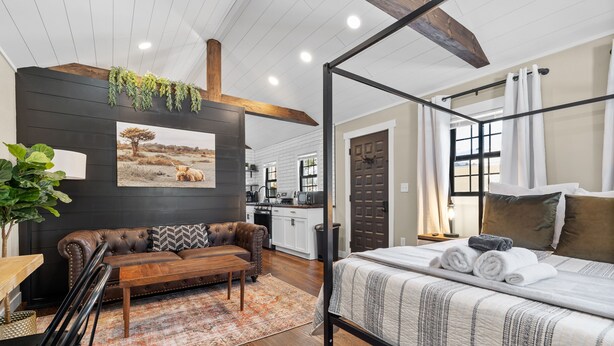 A bedroom with a four-poster bed, a wooden bench, a leather sofa, and a dining table. - Spearfish Cottages (Spearfish)