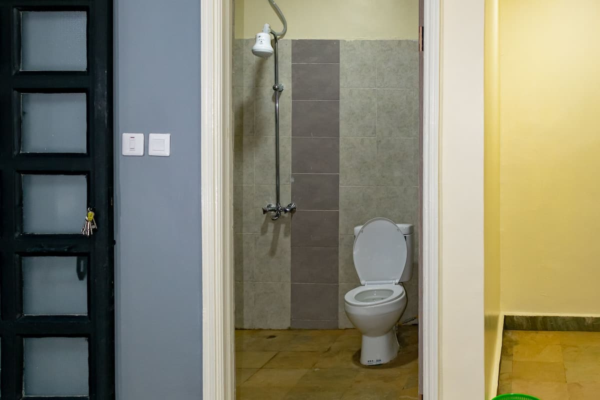 A hotel room with a bed, a bathroom with a toilet and shower, and a green basket on the floor.