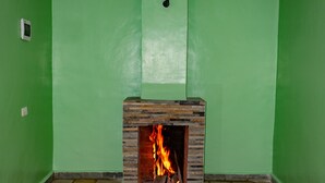Una habitación con paredes verdes, una chimenea de piedra con fuego y un piso de baldosas.