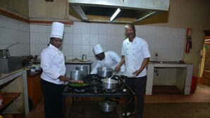 Una cocina profesional con cocineros preparando alimentos, equipo de cocina de acero inoxidable y paredes con azulejos.