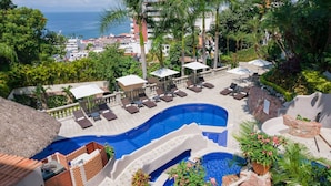 Zona de piscina en un resort con múltiples tumbonas, una piscina pequeña y una cascada.