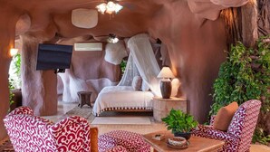 Un dormitorio acogedor con cama, televisión y zona de estar con cojines estampados.