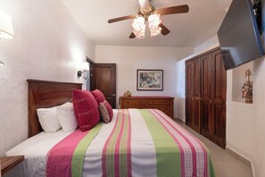 A bedroom with a bed, wooden wardrobe, ceiling fan, and artwork on the wall.