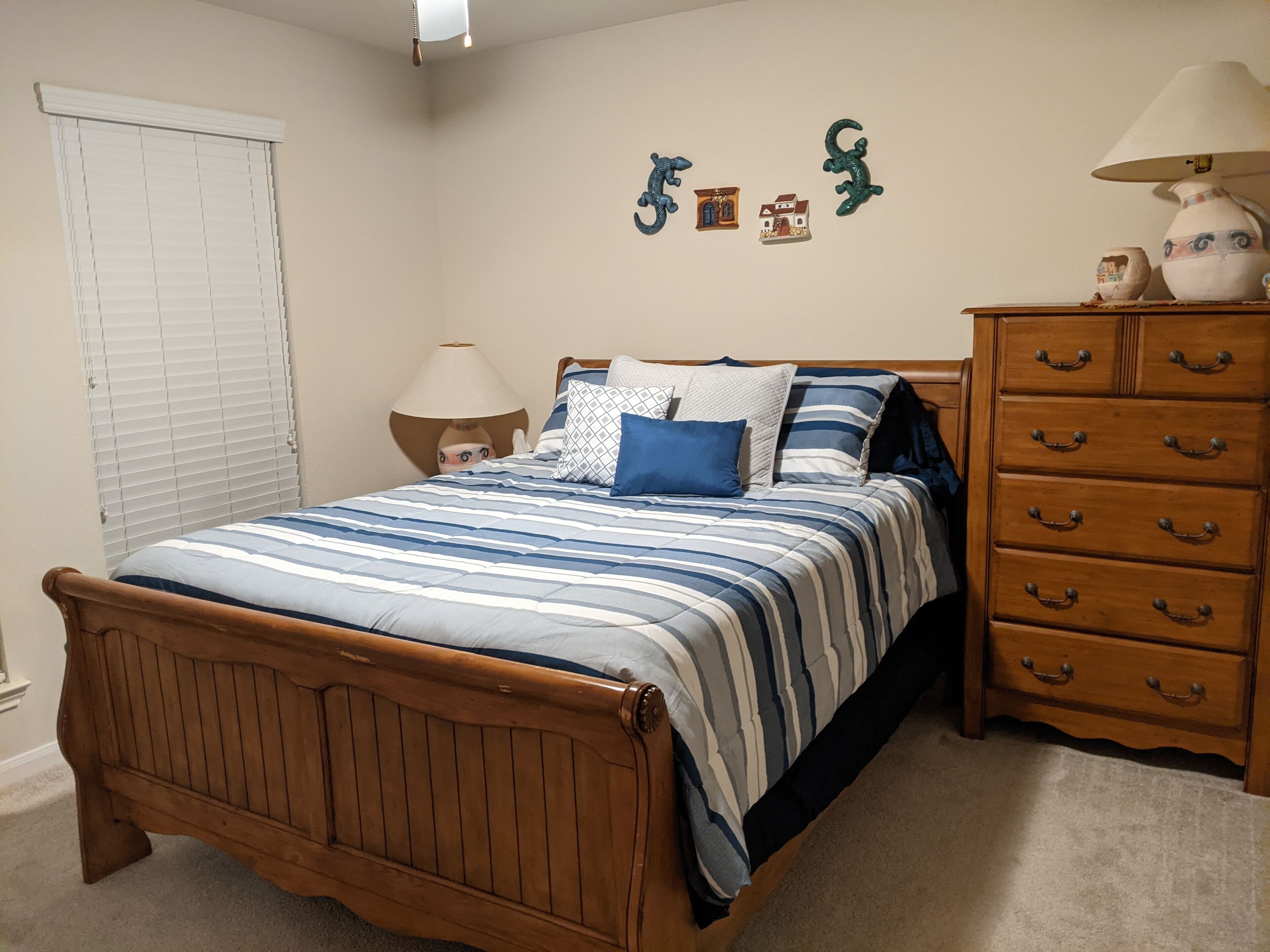 A bedroom with a wooden bed, a dresser with multiple drawers, a nightstand, and wall decorations.