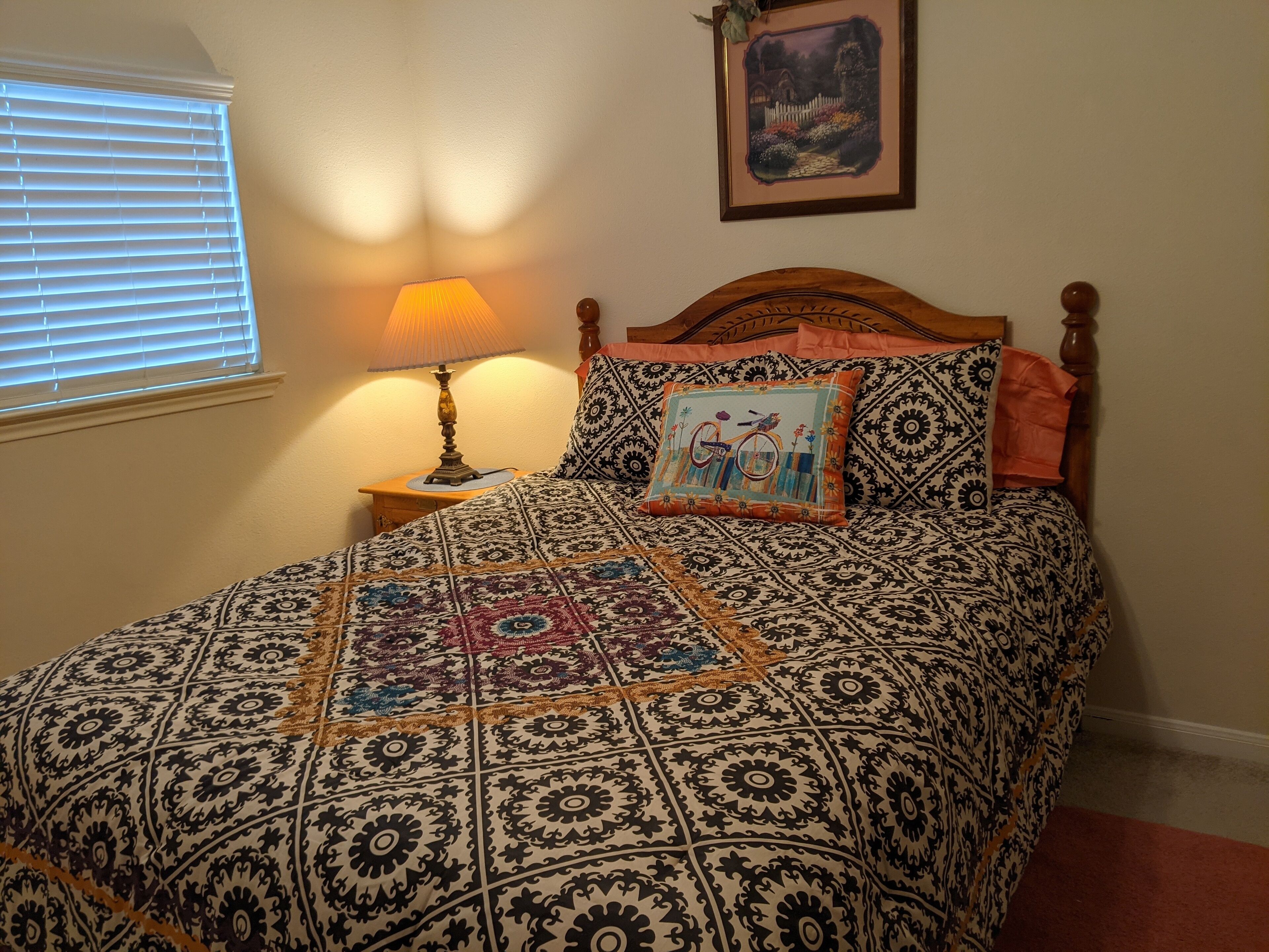 A neatly made bed with a patterned bedspread, a decorative pillow, and a bedside lamp.
