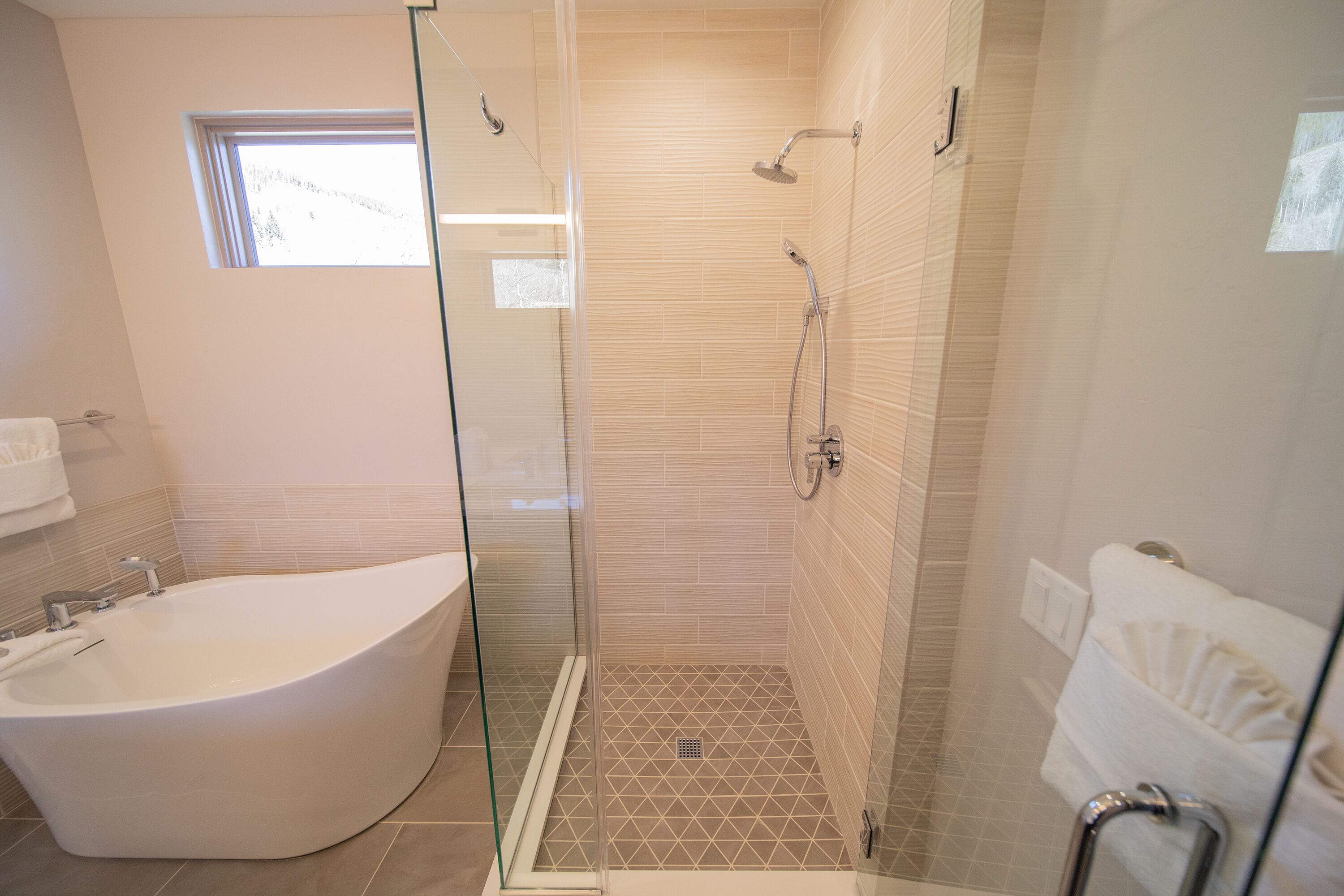A modern bathroom with a glass-enclosed shower, a freestanding bathtub, and a small window providing natural light.
