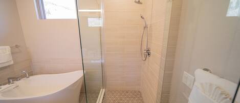 A modern bathroom with a glass-enclosed shower, a freestanding bathtub, and a small window providing natural light.
