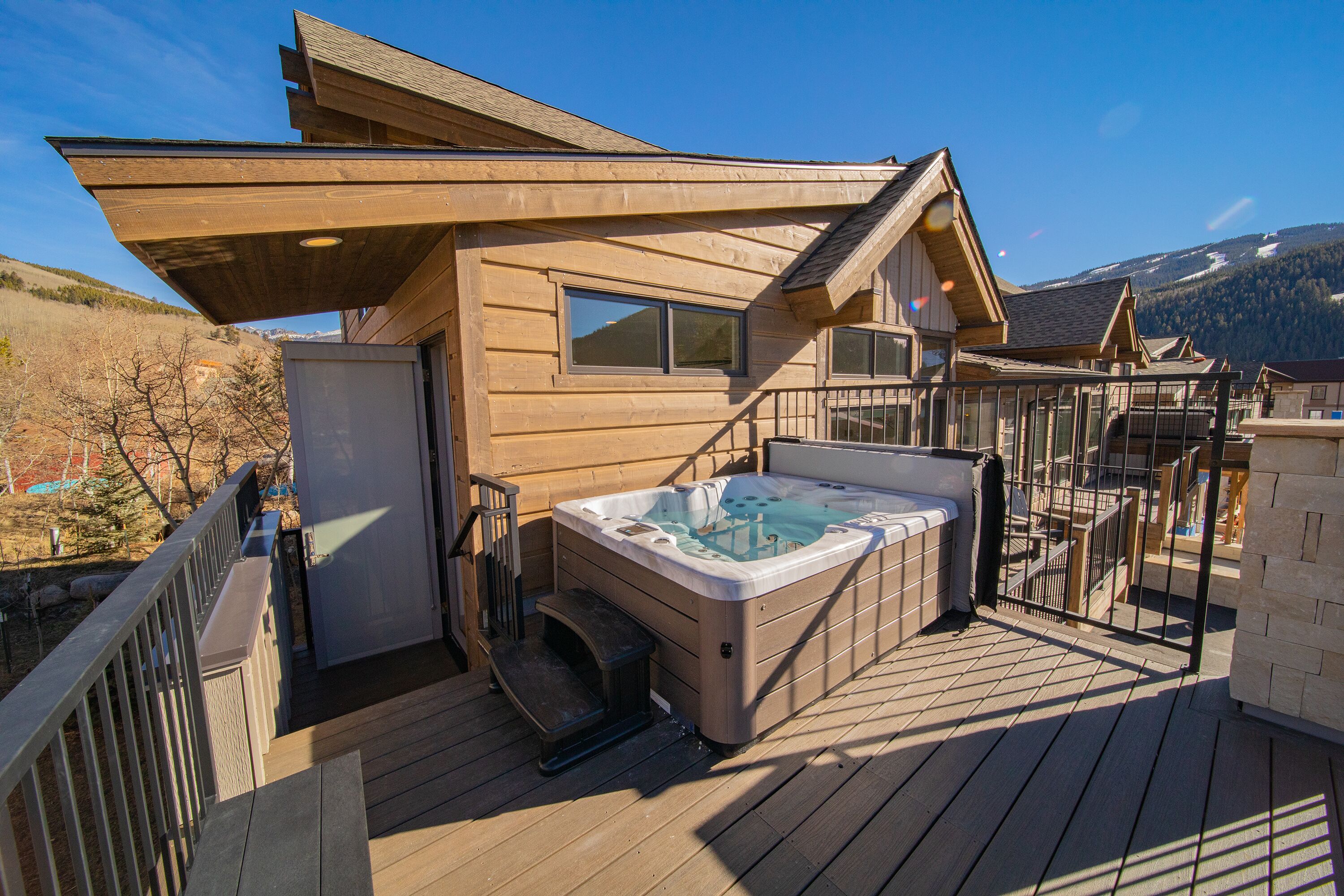 Une cabane en bois avec un jacuzzi sur une terrasse, entourée de montagnes.