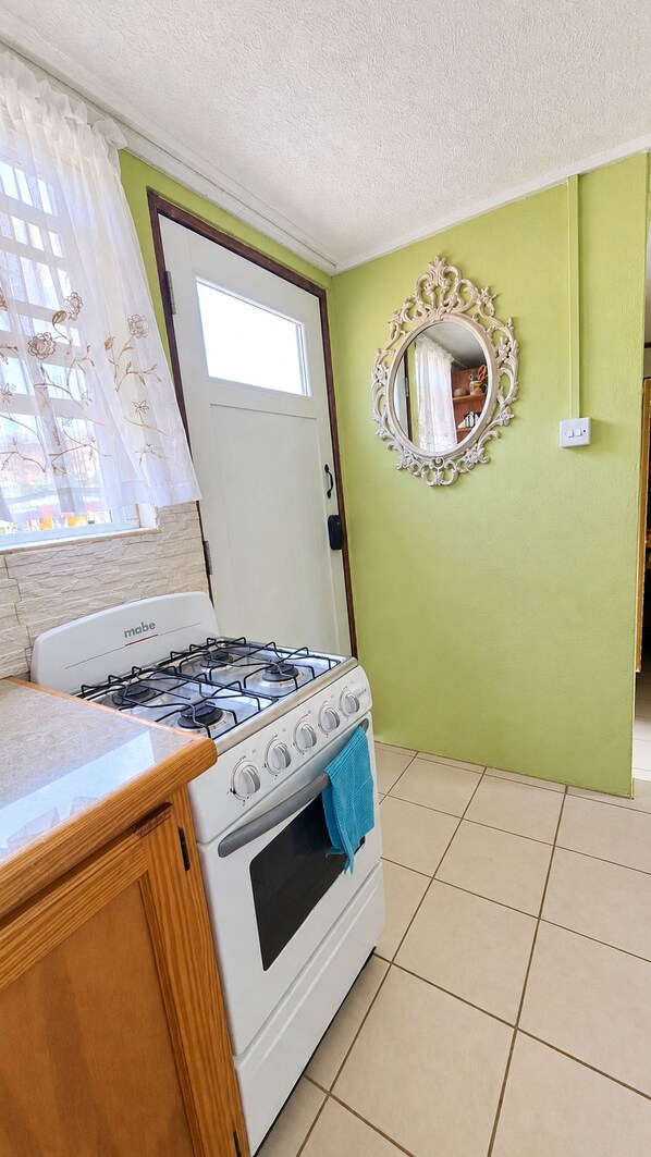 A kitchen with a gas stove, a white oven, a wooden countertop, a mirror with an ornate frame, and a green wall.