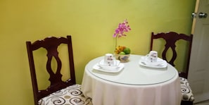 Une table à manger avec deux chaises, un vase de fleurs et un saladier de fruits.