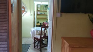 Un couloir mène à une salle à manger équipée d’une table et de chaises, d’un buffet en bois et d’un téléviseur fixé au mur.