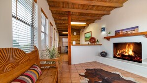A cozy living room with a wooden ceiling, a fireplace, a sofa with a colorful cushion, and a cowhide rug. - Pecos Trail Inn (Santa Fe)