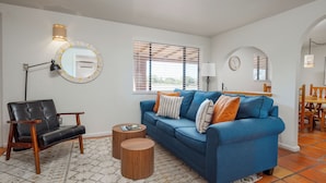 A living room with a blue sofa, a black leather chair, a round mirror, and a small wooden coffee table. - Pecos Trail Inn (Santa Fe)