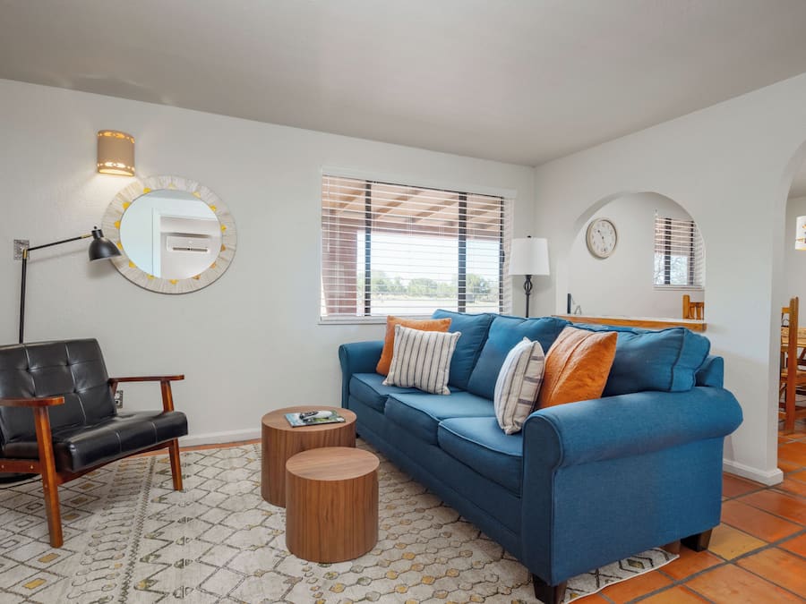 A living room with a blue sofa, a black leather chair, a round mirror, and a small wooden coffee table.