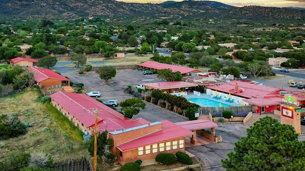 A hotel with multiple red-roofed buildings, a swimming pool, and a mountainous backdrop. - Pecos Trail Inn (Santa Fe)