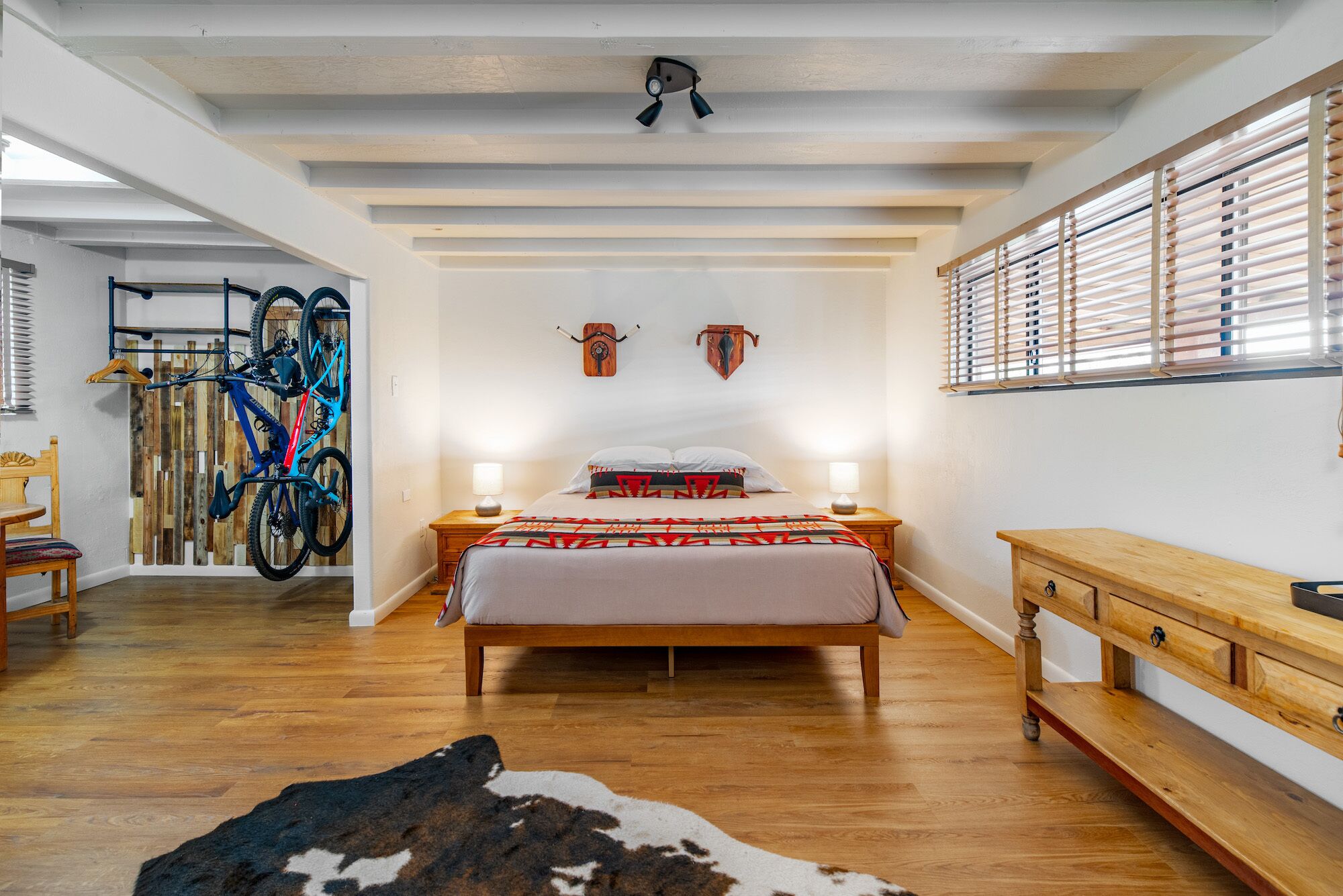 Un dormitorio con una cama de madera, dos lámparas de noche, un banco de madera y un soporte para bicicleta en la pared.