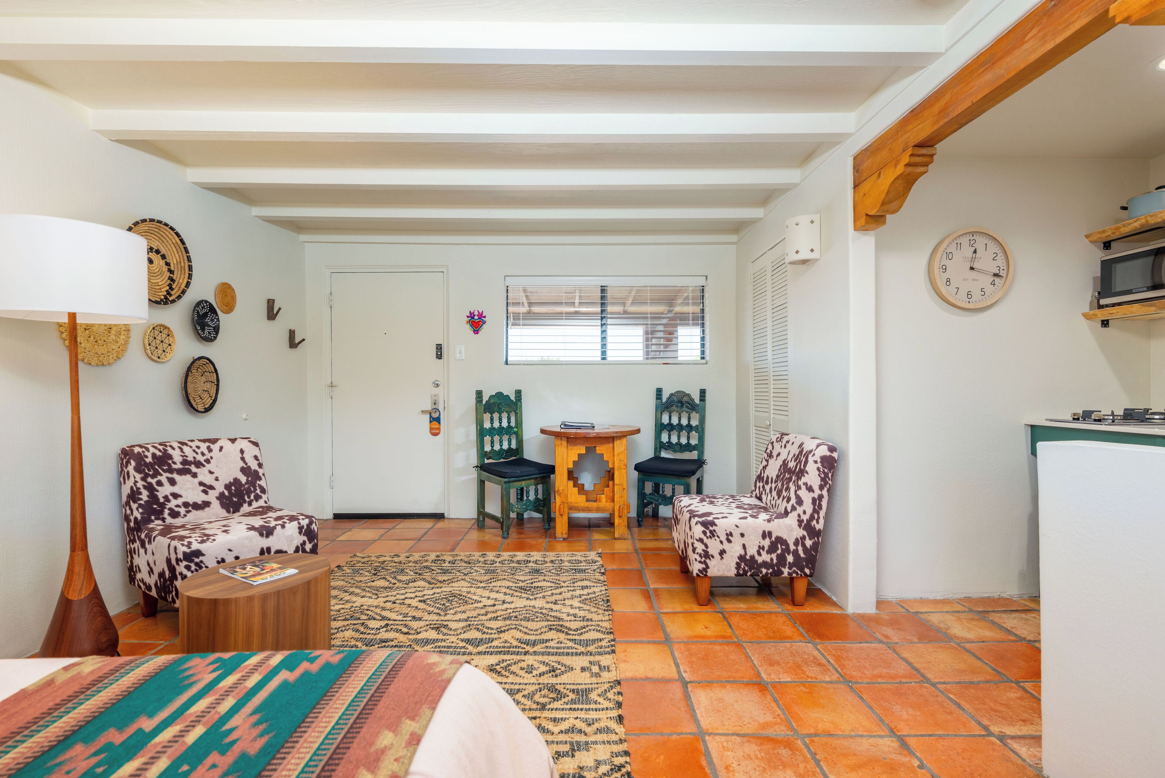 A living room with a sofa, chairs, a coffee table, a lamp, a patterned rug, and a kitchen area with a microwave.