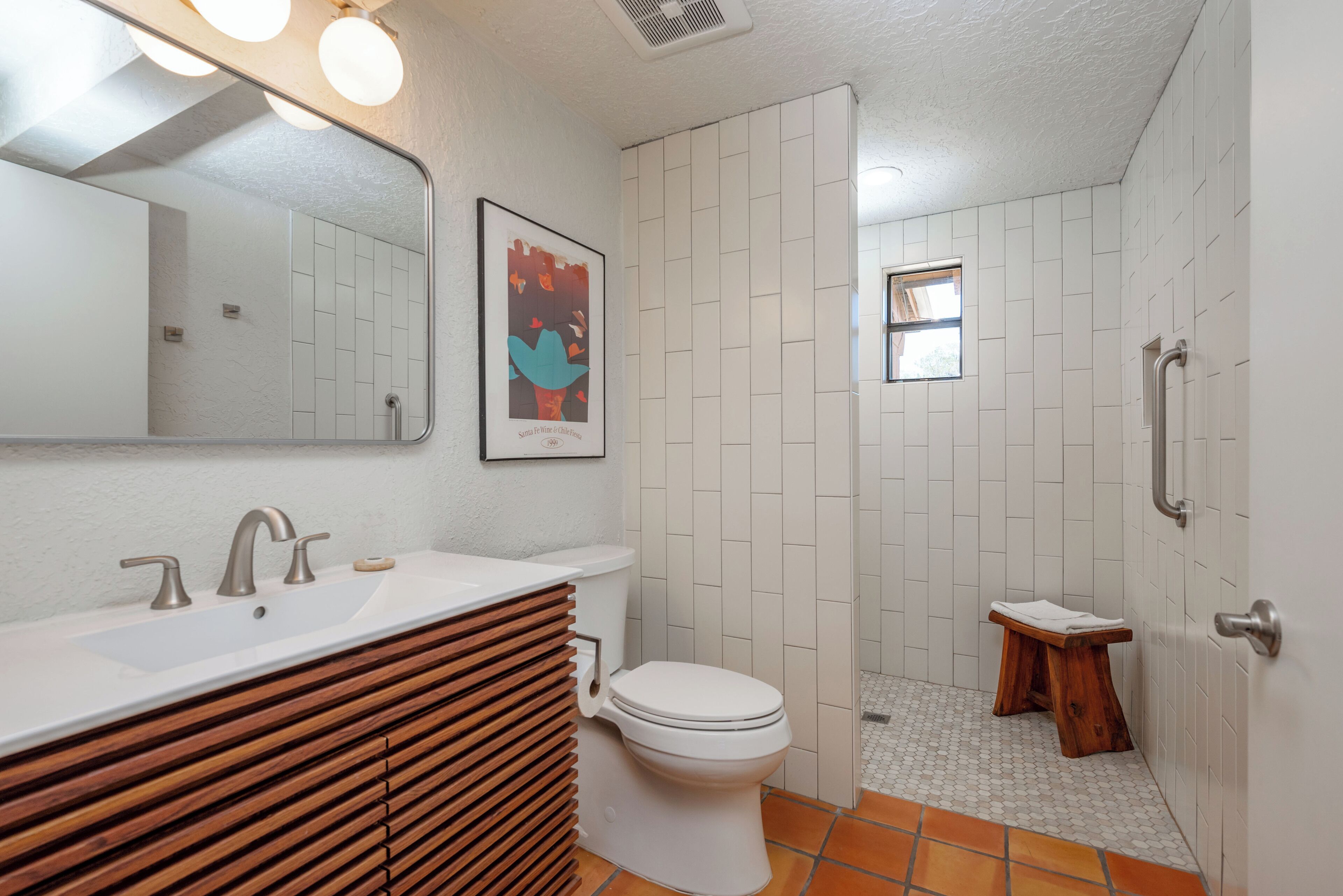 A bathroom with a white sink, wooden vanity, a toilet, and a shower area.
