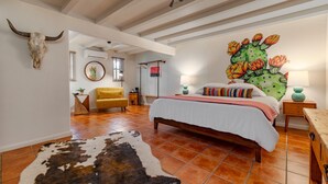 A bedroom with a bed, a cowhide rug, a cactus mural, and a bull skull on the wall. - Pecos Trail Inn (Santa Fe)
