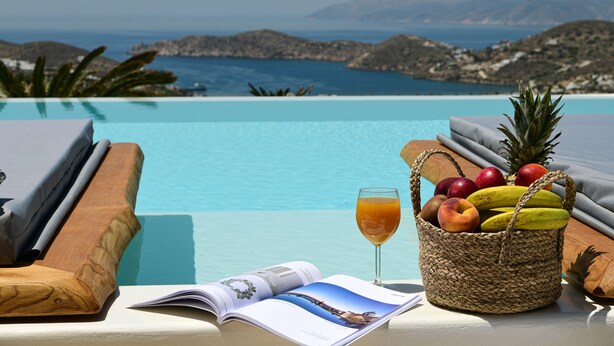 En utsikt över poolen med en korg full av frukt, ett glas juice och en tidning.