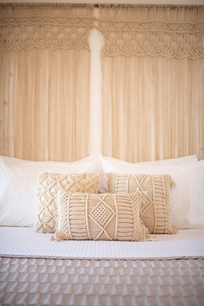A bed with white bedding and two macramé pillows.
