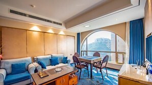 Une chambre d’hôtel moderne, dotée d’un canapé, d’une table à manger avec des chaises, d’une petite table d’appoint en bois et d’une grande fenêtre offrant une vue panoramique.