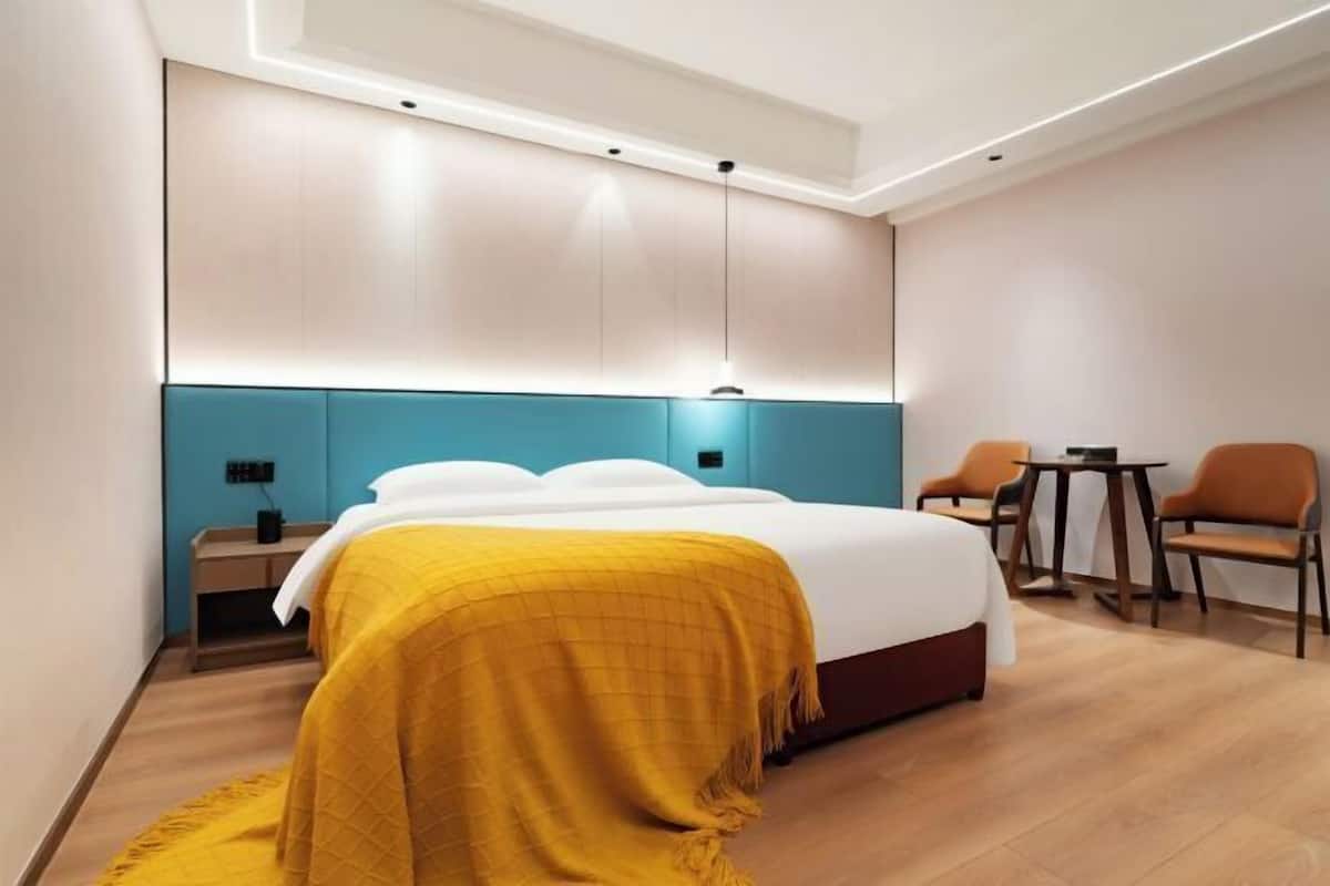 A modern hotel room with a large bed, a desk, two chairs, and a small table.